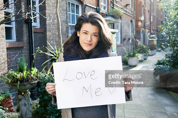 woman holding sign saying "love me" - placard foto e immagini stock