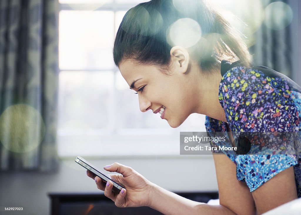 Woman on bed smiling and looking at mobile phone