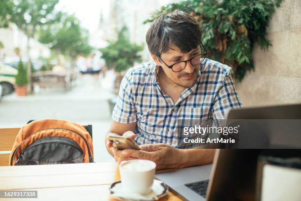 man with smart phone working on laptop in a sidewalk cafe in summer - georgian man stock pictures, royalty-free photos & images