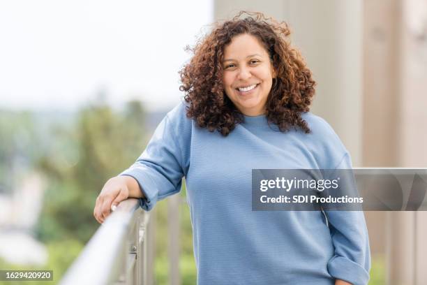 mid adult woman stands on balcony of city apartment - midwest usa stock pictures, royalty-free photos & images