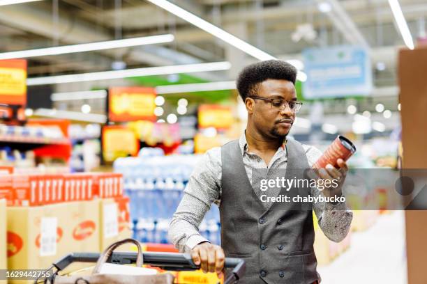 man reads nutrition labels while shopping - food labels stock pictures, royalty-free photos & images