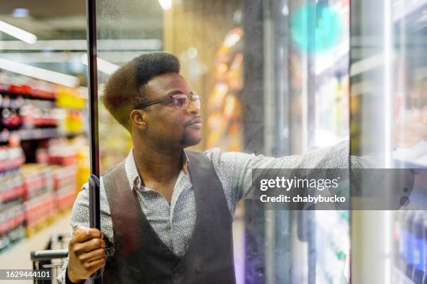 man choosing cold drink from fridge in supermarket - refrigerated section supermarket stock pictures, royalty-free photos & images