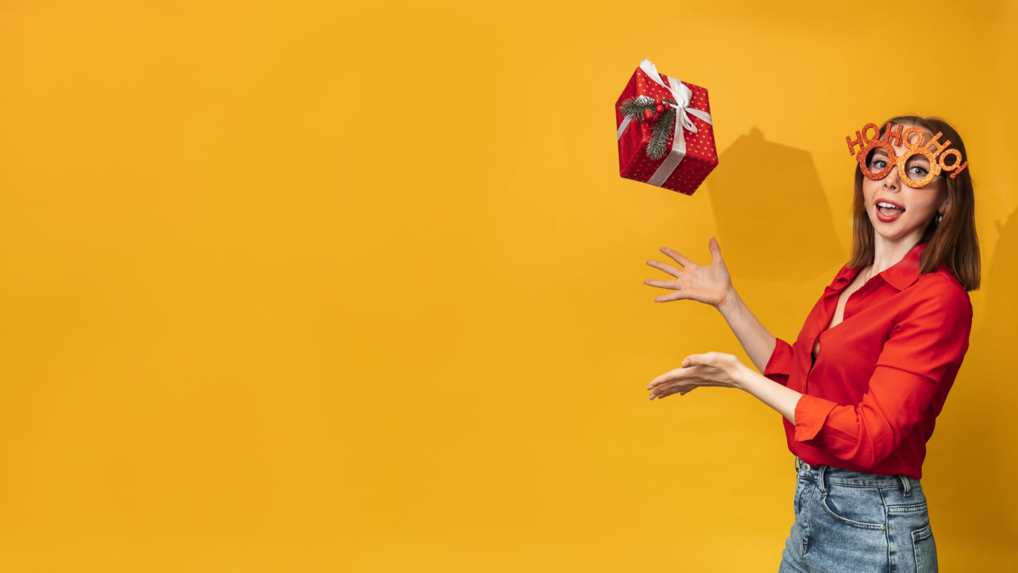 A young woman tosses a Christmas box in her hands on a yellow background. The concept of celebrating Christmas and New Year. A place for your text. A young woman tosses a Christmas box in her hands on a yellow background. The concept of celebrating Christmas and New Year. A place for your text.