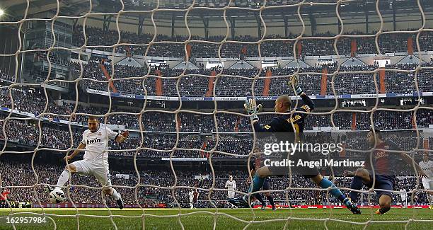 Karim Benzema of Real Madrid scores the opening goal past goalkeeper Victor Valdes and Javier Mascherano of Barcelona during the La Liga match...