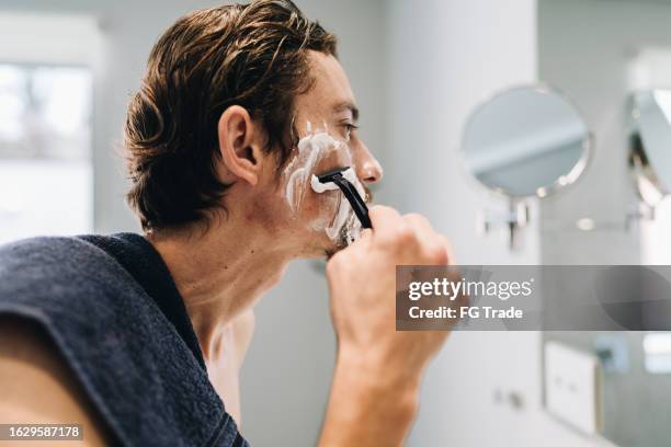 mid adult man shaving his face in the bathroom at home - man shaving foam stock pictures, royalty-free photos & images