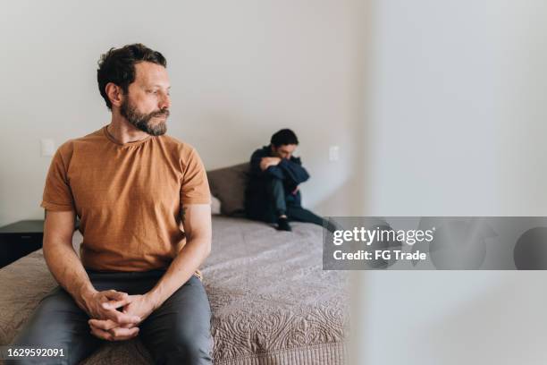 worried father sitting in the bed after fighting with his son at home - awkward family photo stock pictures, royalty-free photos & images