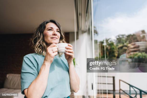 contemplative mature woman looking throught the window at home - balkong bildbanksfoton och bilder