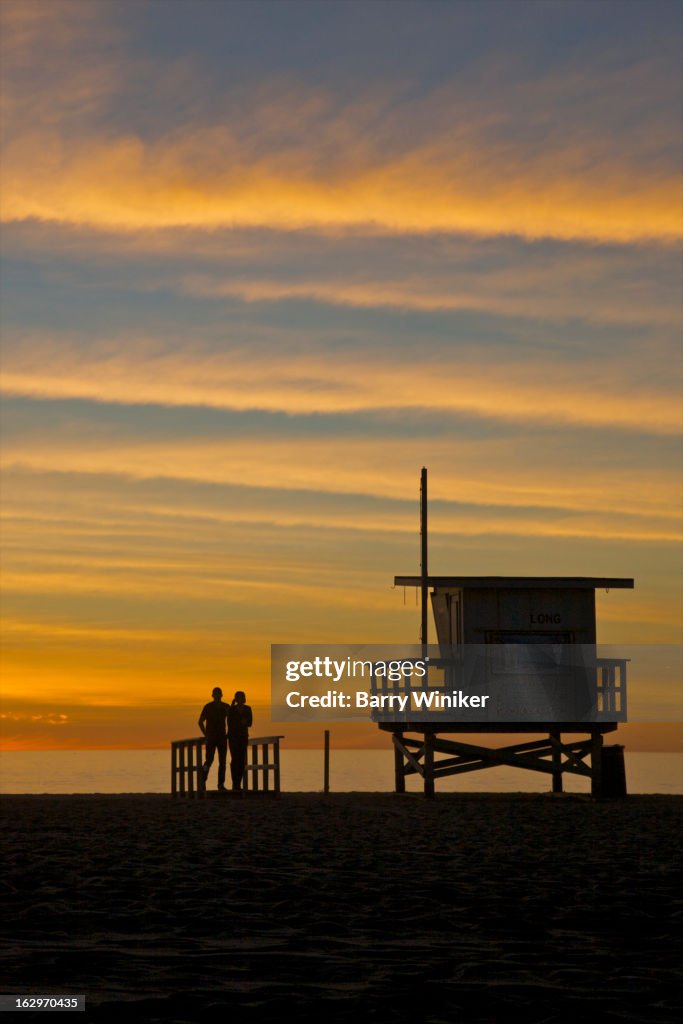 Silhouetted couple under colorful dusk skies.