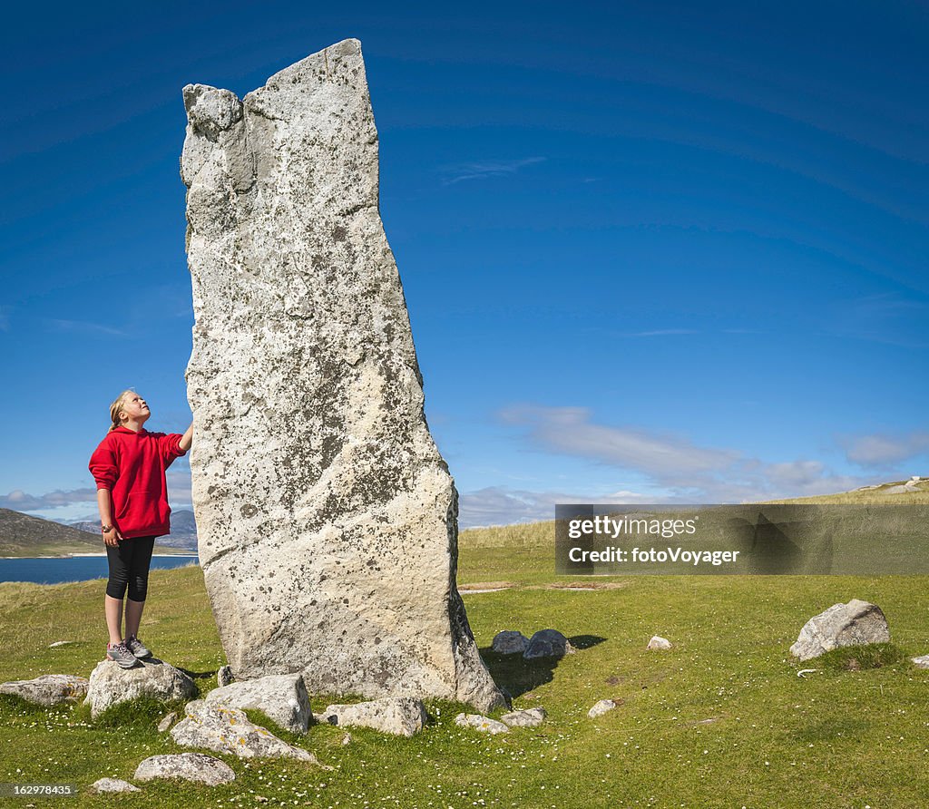 Girl looking up at ancient stone monolith Outer Hebrides Scotland