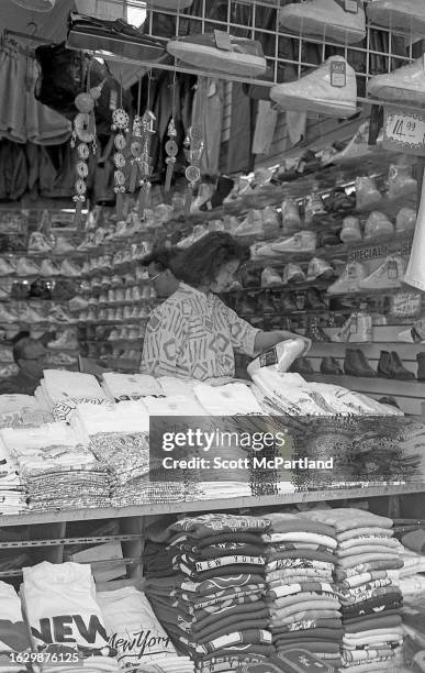 View of a customer examining sneakers at a open air stall on Canal Street , in the Chinatown neighborhood, New York, New York, May 19, 1990.