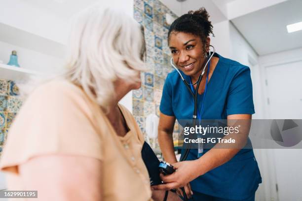 nurse taking blood pressure of a senior woman at home - happiness meter stock pictures, royalty-free photos & images