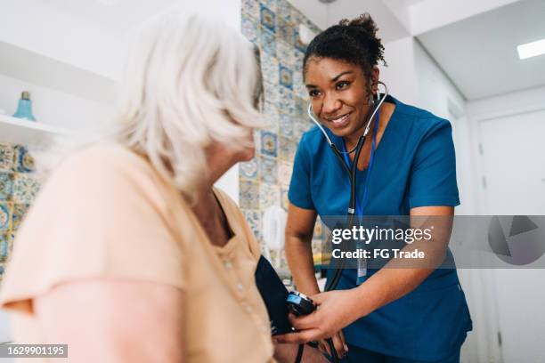 nurse taking blood pressure of a senior woman at home - high blood pressure gauge stock pictures, royalty-free photos & images