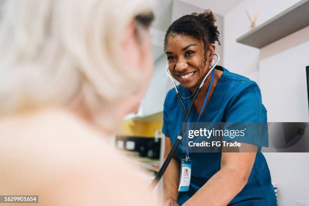 nurse taking blood pressure of a senior woman patient at home - nurse stock pictures, royalty-free photos & images