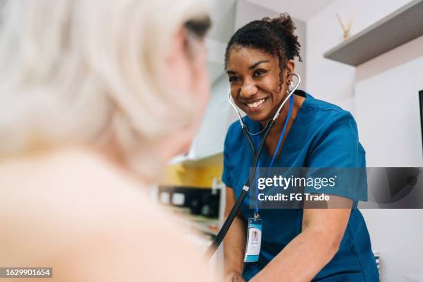 nurse taking blood pressure of a senior woman patient at home - nursing assistant stock pictures, royalty-free photos & images