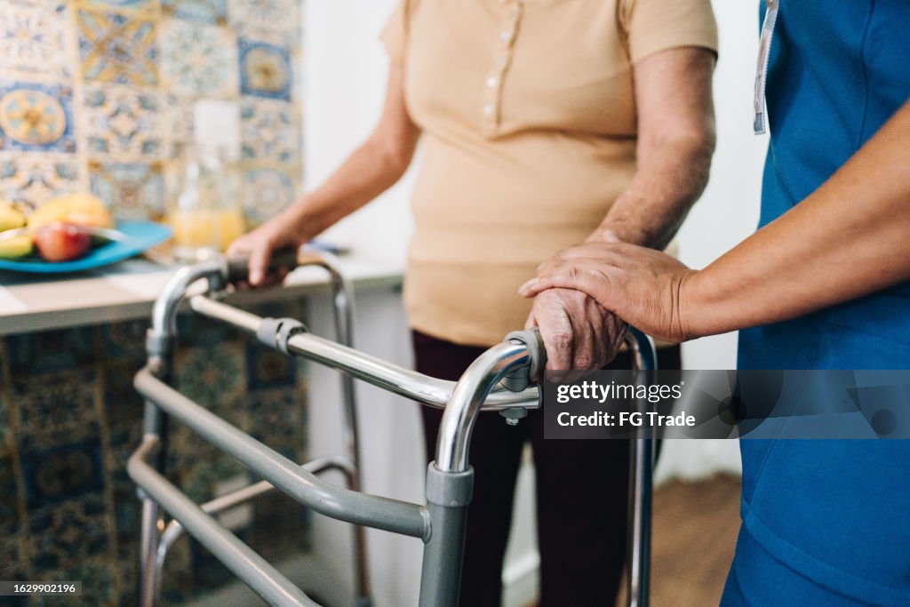 Häusliche Pflegekraft hilft einer älteren Frau, die zu Hause spazieren geht