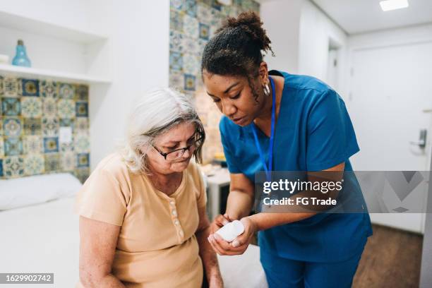 home caregiver explaining to senior woman how to take her medicine at home - nursing assistant stock pictures, royalty-free photos & images