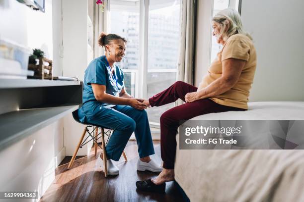 nurse massaging a senior woman's foot at home - old lady feet stockfoto's en -beelden