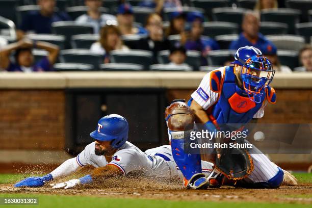 Ezequiel Duran of the Texas Rangers slides safely into home plate before catcher Omar Narvaez of the New York Mets gets the ball to score the go...