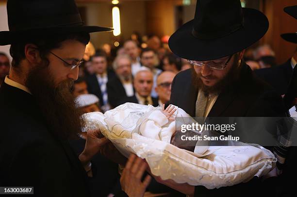 Orthodox Jews pass baby infant Mendl Teichtal to one another before his circumcision at the Chabad Lubawitsch Orthodox Jewish synagogue on March 3,...