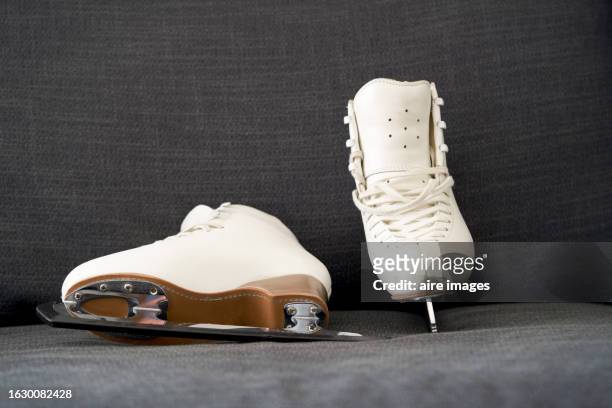 side view of a pair of white figure skating boots on the ground with metal blades, no people around. - figure skating pair stock pictures, royalty-free photos & images