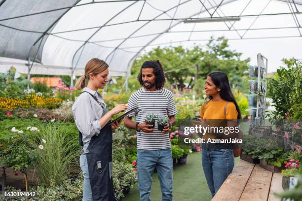 a female garden center worker educating a diverse young couple on plants at a garden center - botanist stockfoto's en -beelden