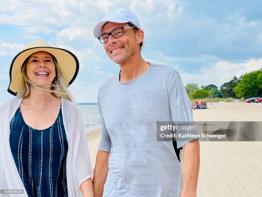 Young at heart senior couple having fun together walking on beach against stormy sky