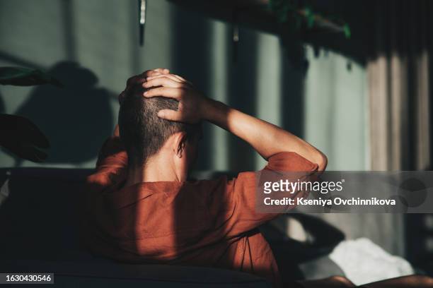unpleasant pain. sad unhappy handsome man sitting on the sofa and holding his forehead while having headache - depresión económica fotografías e imágenes de stock