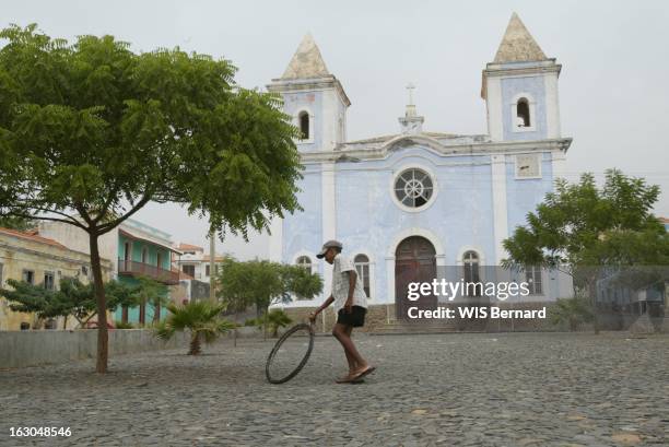 The Cape Verde Islands. Ile de Fogo : enfant jouant au cerceau avec une roue de vélo devant l'église adventiste de São Filipe.