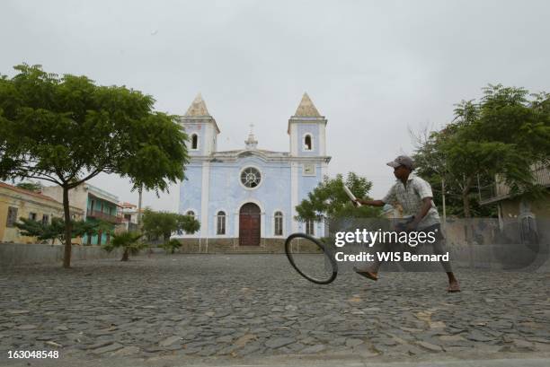 The Cape Verde Islands. Ile de Fogo : enfant jouant au cerceau avec une roue de vélo devant l'église adventiste de São Filipe.