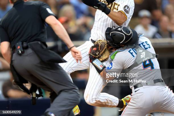 Nick Fortes of the Miami Marlins is hit in the head during a collision at home plate with Fernando Tatis Jr. #23 of the San Diego Padres during the...