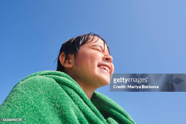 an asian boy is drying himself after swimming in the sea, wrapped in a green towel against a blue sky. - only kids at sky stockfoto's en -beelden