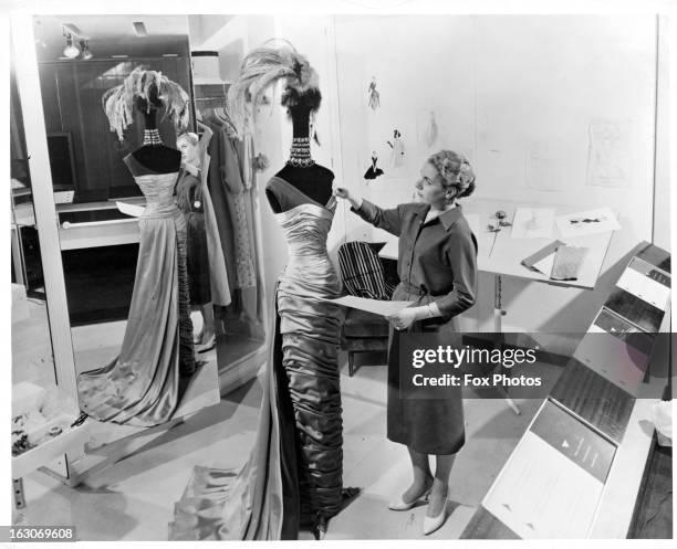Here can be seen an assistant putting the finishing touches to the ball gown designed by Norman Hartnell at a couturier studio in Belgium, 1955.