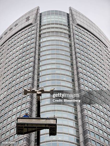 Maintenance workers stand on a suspended platform in front of Mori Building Co.'s Roppongi Hills Mori Tower as they prepare to clean the windows of...