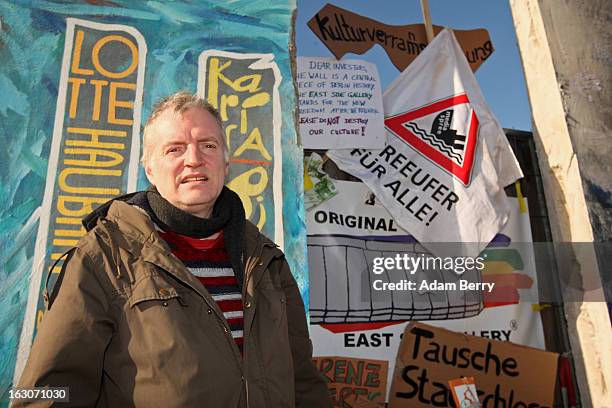 Artist Thierry Noir, who has painted a section of the East Side Gallery, poses in front of posters against the removal of the longest remaining...