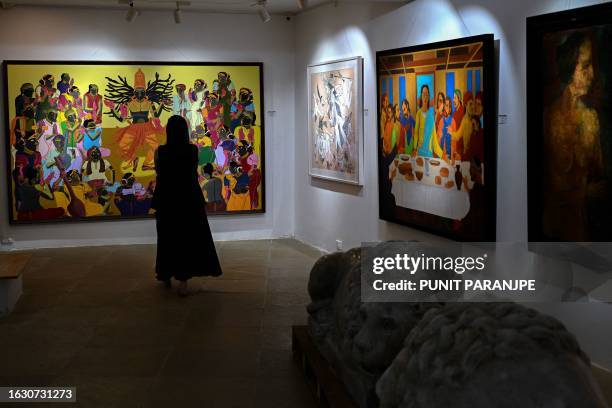 An employee looks at artworks by artists T Vaikuntam , K Laxma Goud and Akbar Padamsee displayed at the AstaGuru auction house gallery ahead of their...