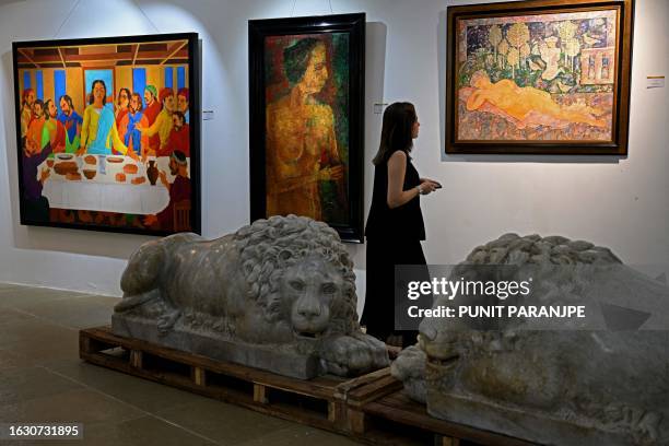 An employee looks at artworks by artists K Laxma Goud , Akbar Padamsee and Sakti Burman displayed at the AstaGuru auction house gallery ahead of...