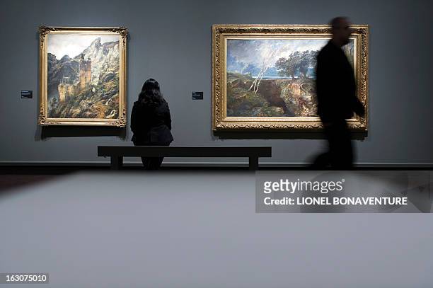 Woman looks at "Paysage montagneux : ruines dans une gorge" painting by Carl Friedrich Lessing and "Le gouffre" painting by Paul Huet, displayed...