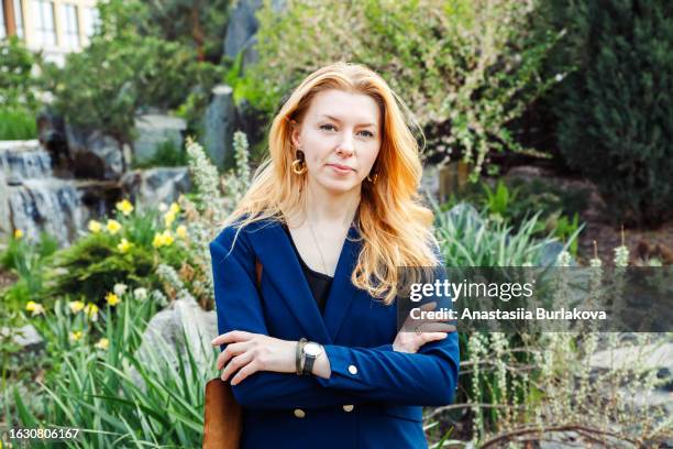 female woman with long orange colored hair with cross arms on chest in garden. architect landscape designer portrait