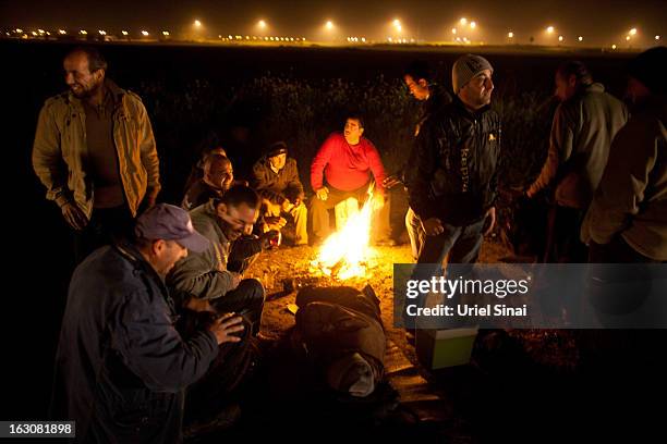 Palestinians warm up by a fire as they wait for a bus as a new line is made available by Israel to take Palestinian labourers from the Israeli army...