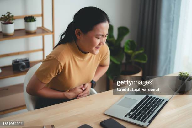 asian woman feeling stomachache sitting at home office. - gastric ulcer stock pictures, royalty-free photos & images