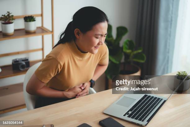 asian woman feeling stomachache sitting at home office. - gastric ulcer 個照片及圖片檔