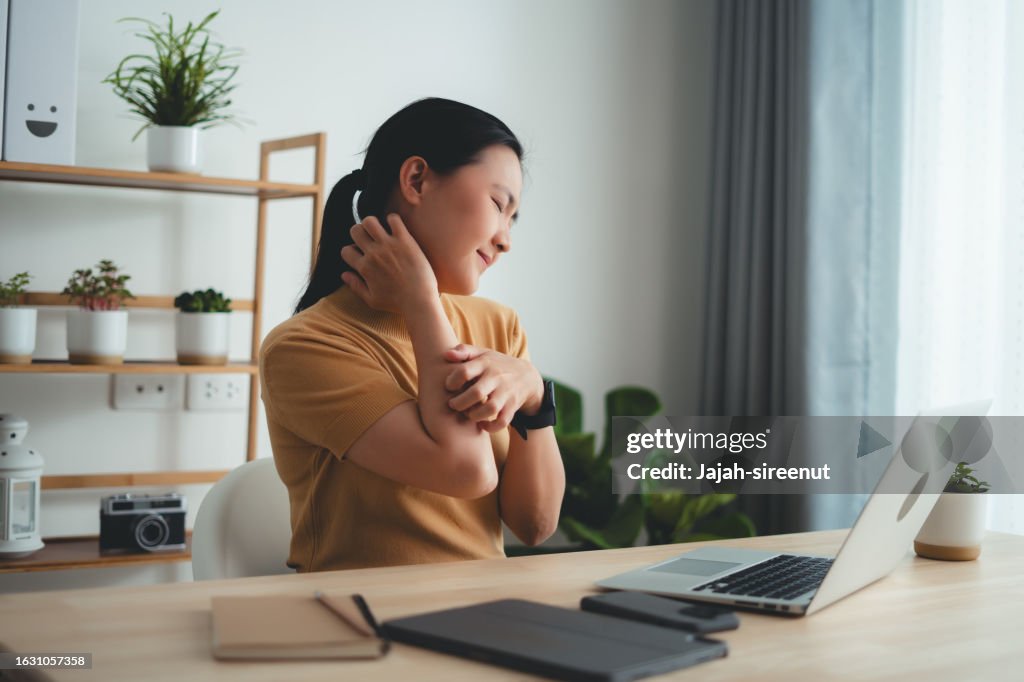 Asian woman irritate itching dry skin scratching her skin sitting at home office.
