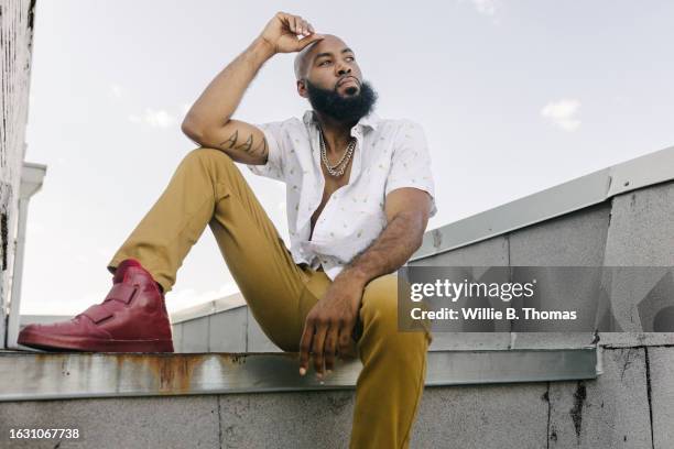 stylish man sitting on ledge during roof party - gold chain necklace stock pictures, royalty-free photos & images
