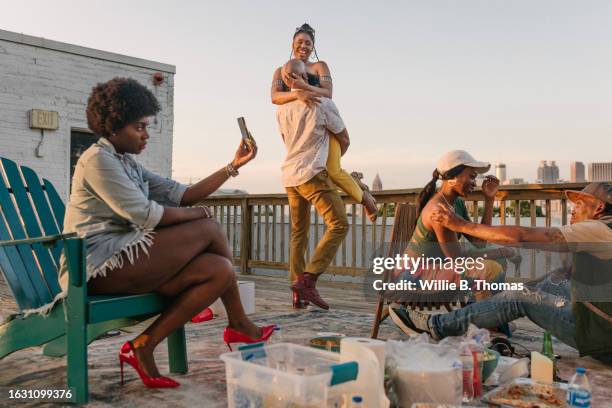 woman taking selfie at rooftop party while friends hang out - african american culture - fotografias e filmes do acervo