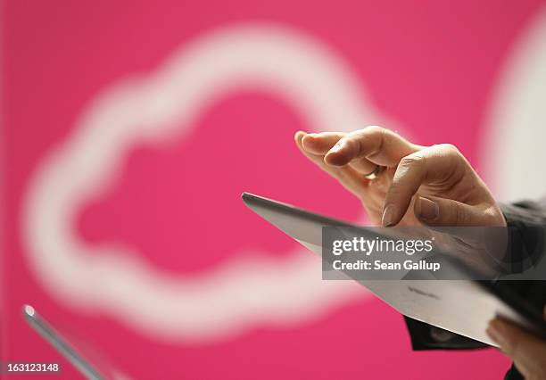 Visitor tries out a tablet computer next to a cloud computing and technology symbol at the Deutsche Telekom stand at the 2013 CeBIT technology trade...