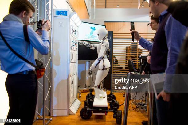 Visitors take pictures of AILA, or Artificial Intelligence Lightweight Android, pressing switches on a panel it recognizes during a demonstration at...