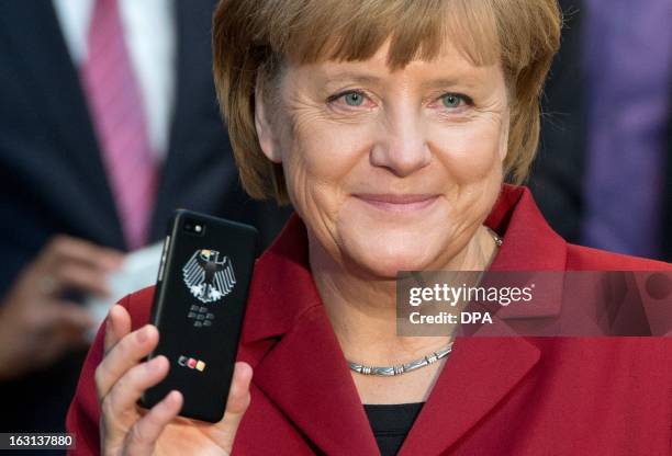 German Chancellor Angela Merkel holds a tapping proof BlackBerry mobile device at the stand of Secusmart as she tours the CeBIT high-tech fair during...