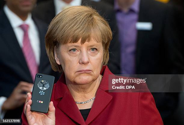 German Chancellor Angela Merkel holds a tapping proof BlackBerry mobile device at the stand of Secusmart as she tours the CeBIT high-tech fair during...