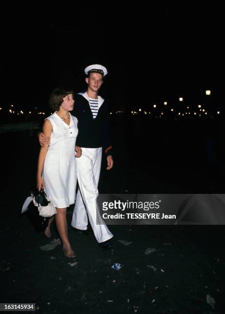 In Paris, 20Th Anniversary Of The Liberation Of August 1944. A Paris, de nuit dans une rue, un marin, en marinière, avec un béret, tenant une jeune...