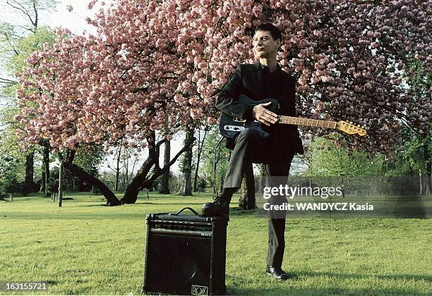 Rendezvous With Etienne Daho. Attitude d'Etienne DAHO avec sa guitare électrique, un pied posé sur l'amplificateur, dans un parc avec un arbre en...